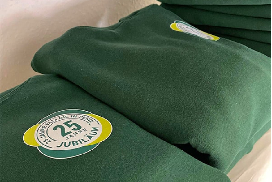 Grüner Pullover mit gesticktem Jubiläumslogo als individuelle Firmenbekleidung.