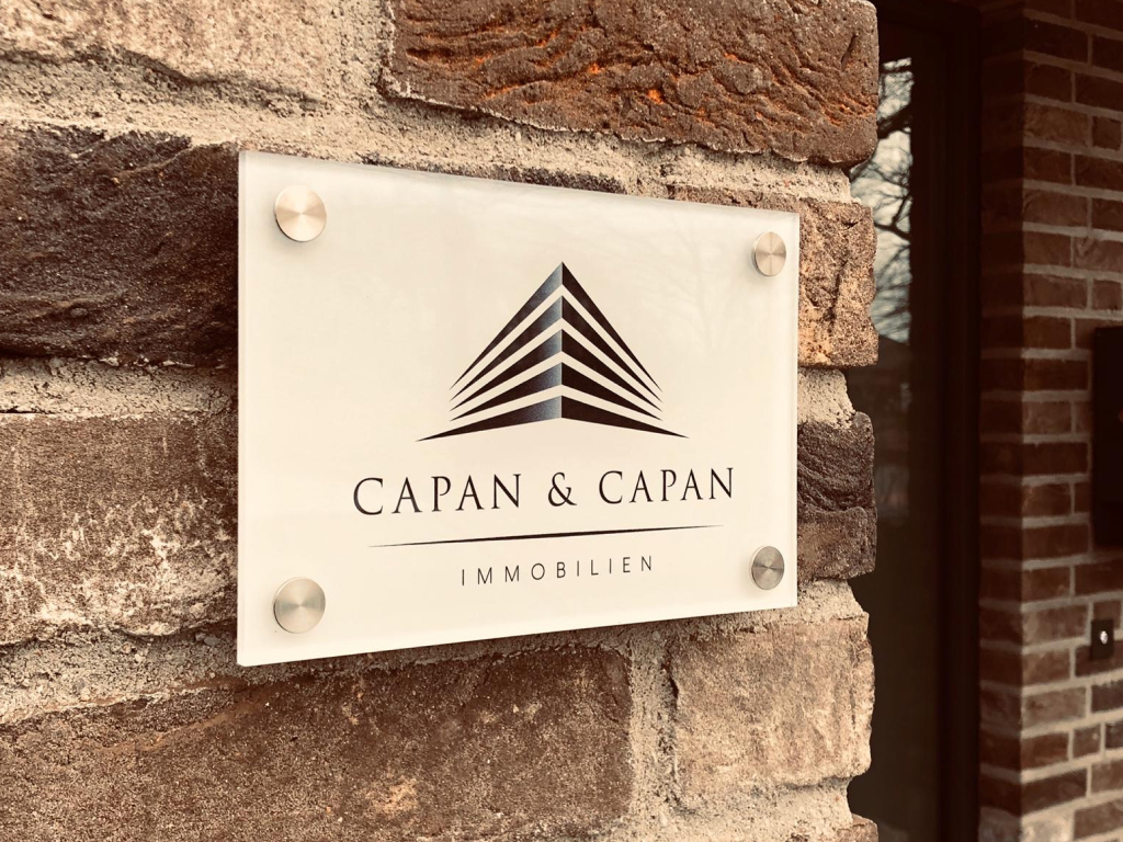 Kleines Glasschild mit Capan & Capan Immobilien Logo als Innenbeschilderung.
